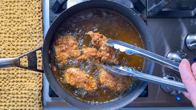 Frying chicken thighs in hot oil in pot on stovetop