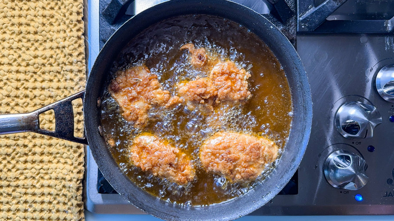 Chicken thighs frying in hot oil in pan on stovetop