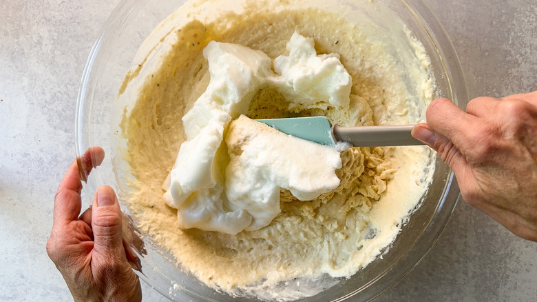 Folding beaten egg whites into waffle batter in glass bowl with spatula