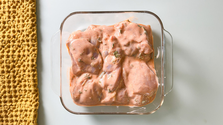 Boneless and skinless chicken thighs marinating in buttermilk brine in glass baking dish