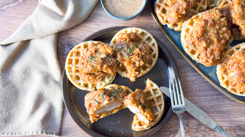 Sweet and savory crispy buttermilk chicken and waffles on plate and serving platter with spicy honey mustard sauce