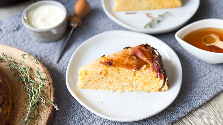 Sweet and savory upside down cornbread slice on plate with butter, honey and fresh thyme