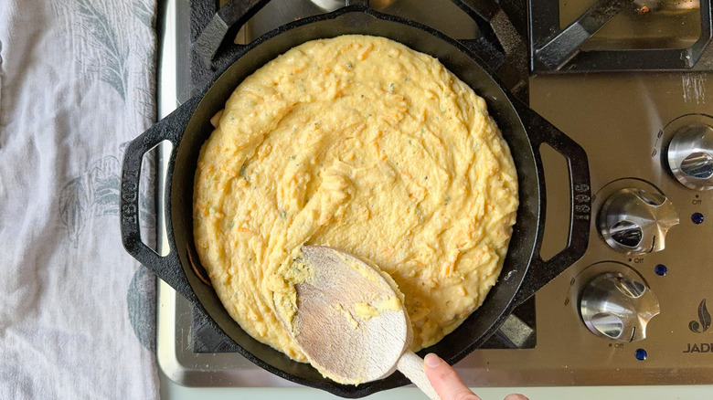 Spreading cornbread batter into cast iron skillet with wooden spoon