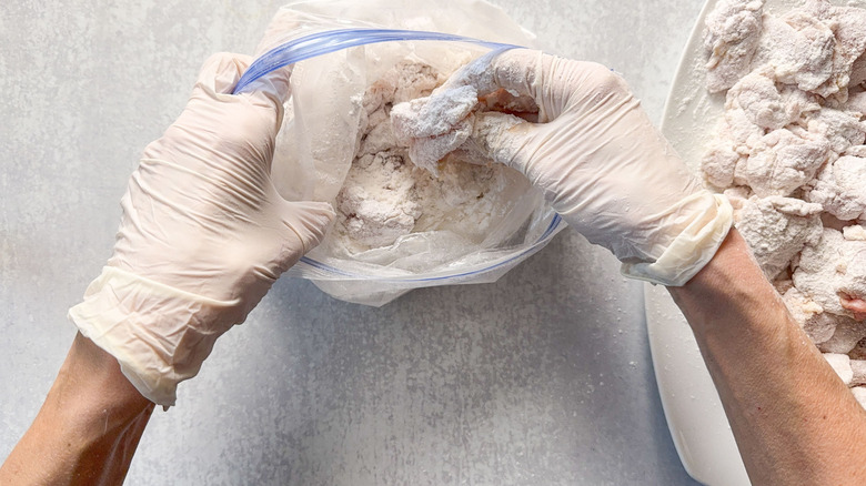 Adding brined chicken thigh pieces to dusting flour in ziplock bag