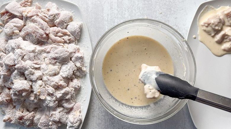 Dipping flour coated chicken thigh pieces in batter with tongs