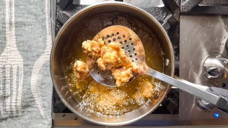 Korean fried popcorn chicken on slotted spoon in pot of avocado oil