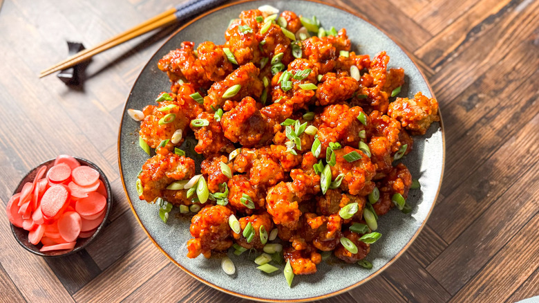 Sweet and spicy Korean fried popcorn chicken on serving platter with pickled radishes, scallions, and chopsticks
