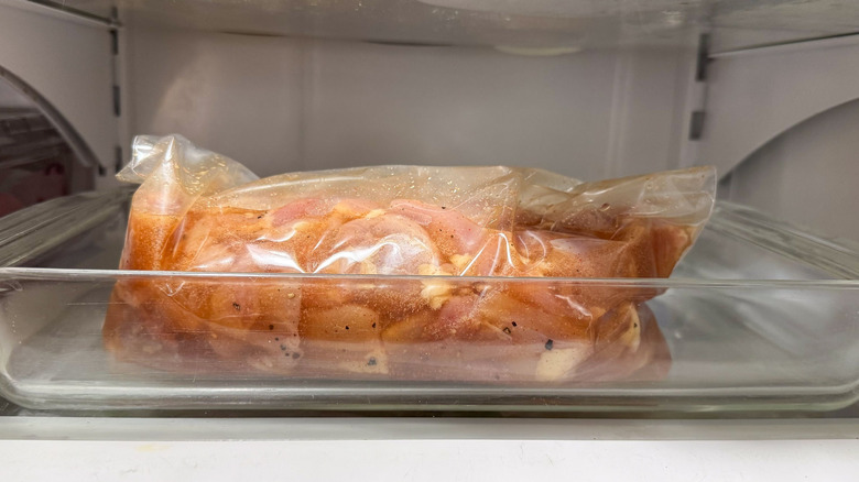 Chicken thigh pieces in brine in Ziploc bag in glass pan in refrigerator