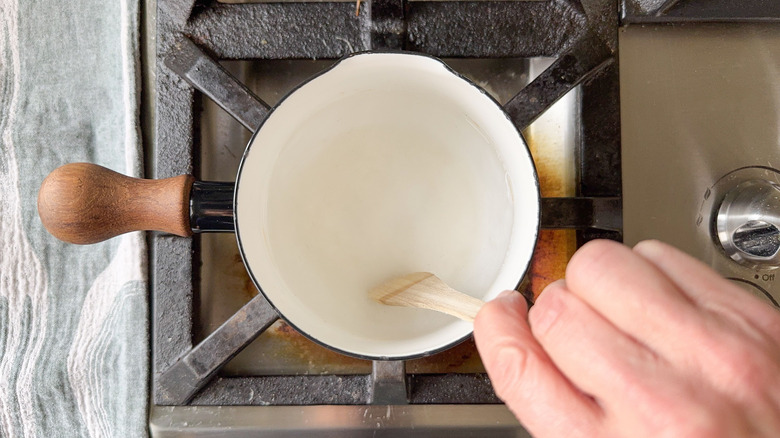Cooking radish pickling brine in saucepan on stovetop with wooden spoon