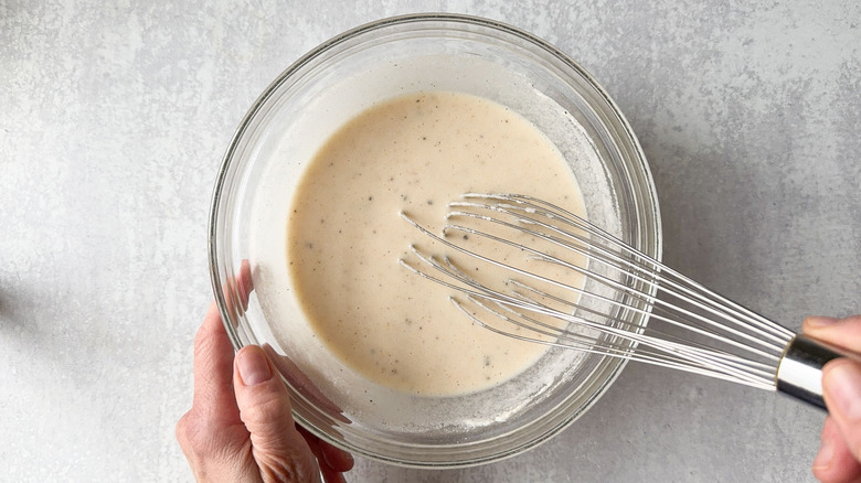 Mixing sweet and spicy Korean fried popcorn chicken batter in glass bowl with whisk