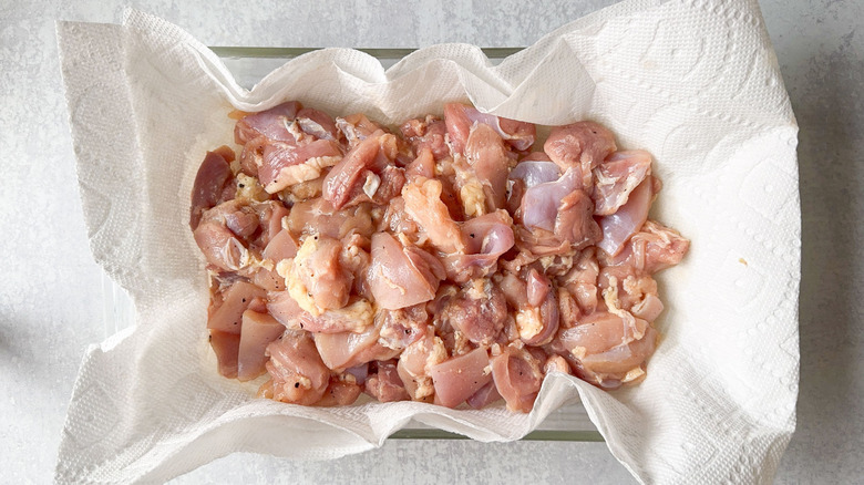 Brined chicken thigh pieces on paper towels in glass dish