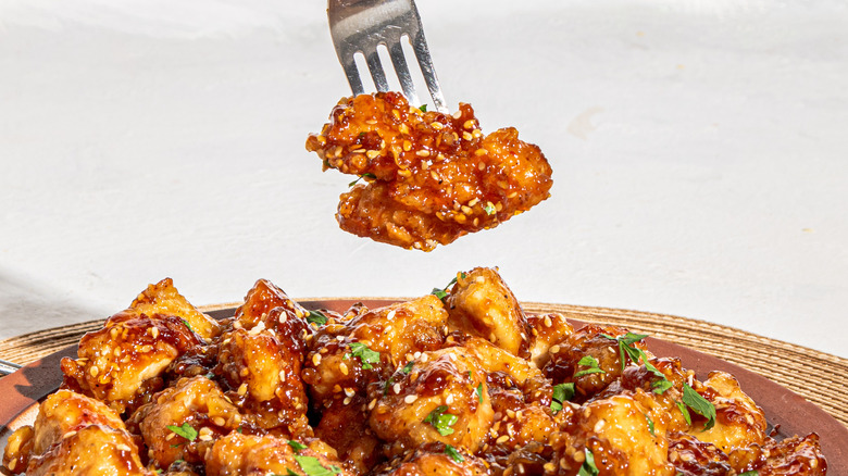 Fork with pieces of glazed chicken over a plate