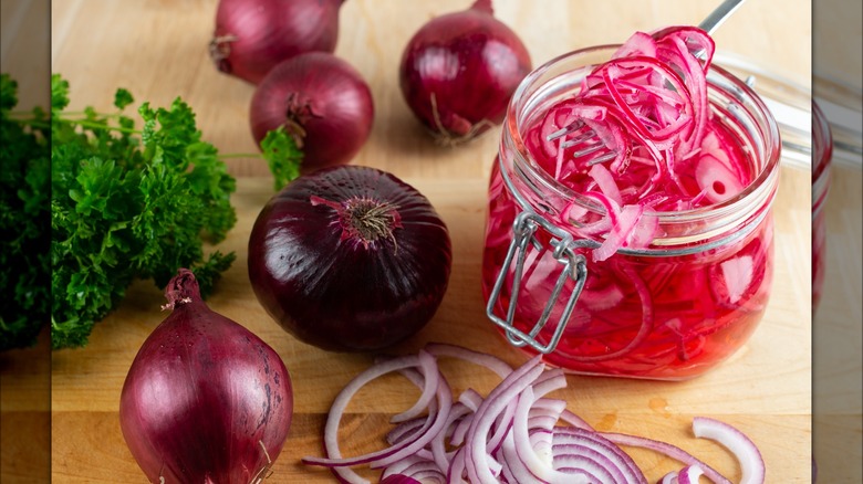 Jar of pickled red onions next to whole and sliced red onions