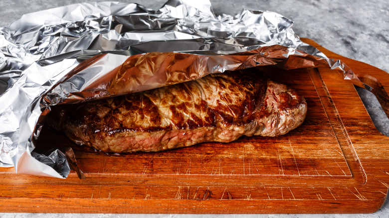 steak resting under tinfoil on cutting board