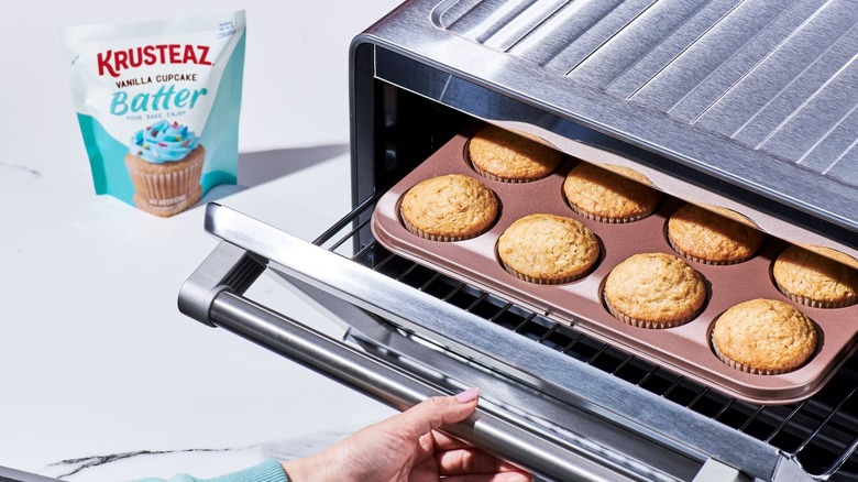 Woman removes freshly baked vanilla cupcakes from oven