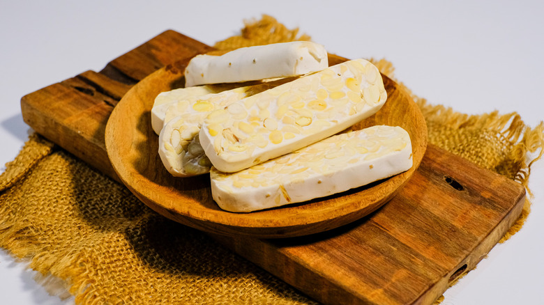 sliced tempeh in a wooden bowl that's placed on a wooden board