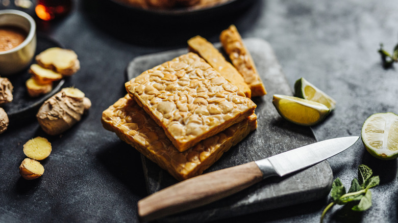 slices of tempeh sit on a cutting board beside a knife and other ingredients