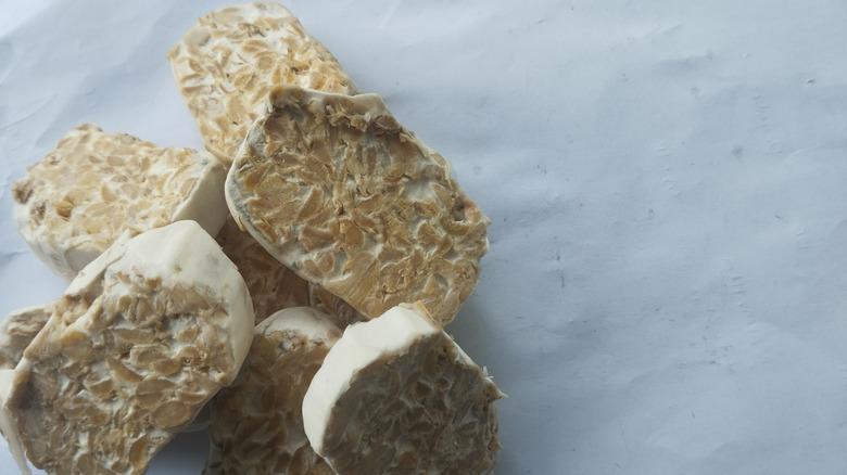 closeup of sliced raw tempeh, rind clearly visible, against a white background