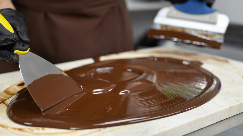 A chocolatier tempers chocolate by spreading it on the tabletop