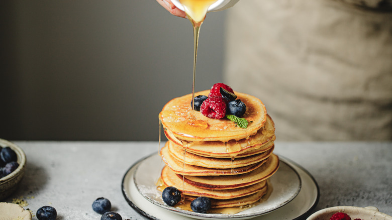 Pouring syrup on pancakes with berries