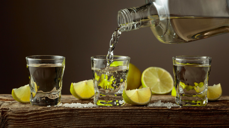 Three shots of tequila being poured surrounded by sliced limes