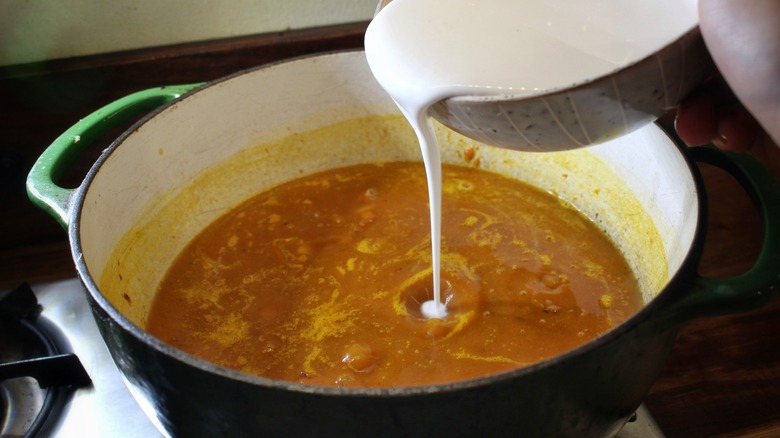 pouring coconut milk into soup