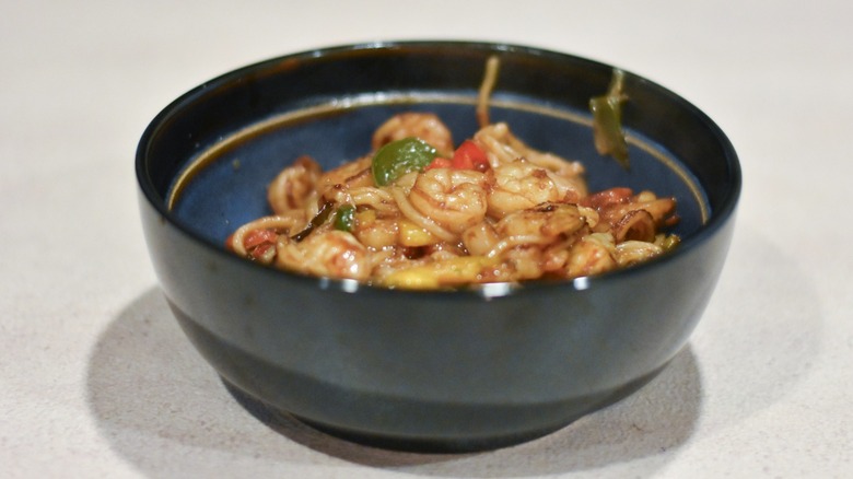 A blue and black bowl with shrimp lo mein on a white counter