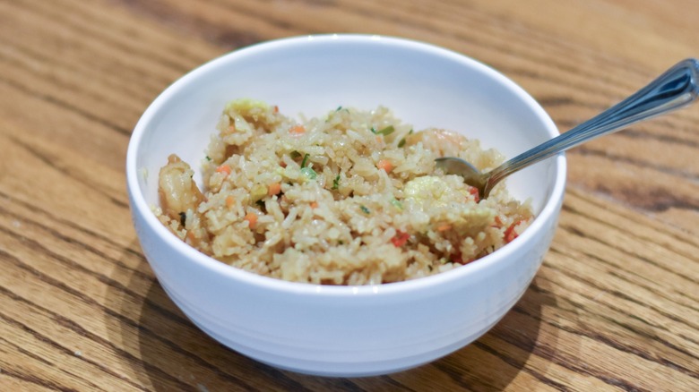 A white bowl with shrimp fried rice on a wooden table