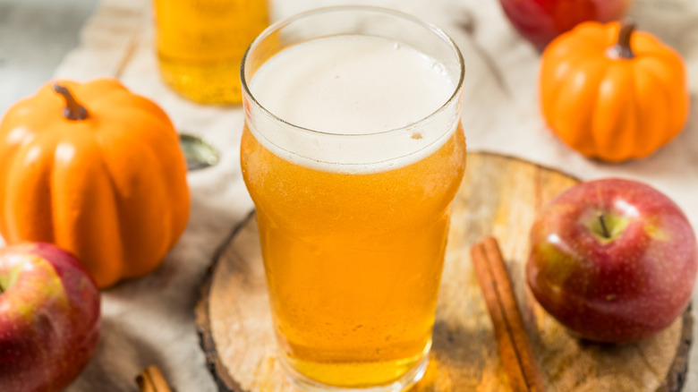 A glass of cider amidst miniature pumpkins, apples and cinnamon sticks