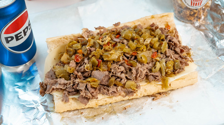 An Italian beef sandwich sits on the paper next to a can of soda.