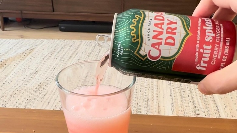 A person pouring a glass of Canada Dry Fruit Splash on a table