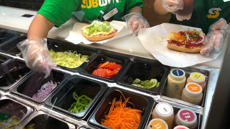 Sandwich artists putting vegetables onto sandwiches