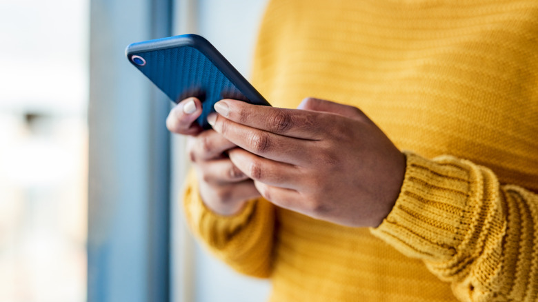 Closeup of woman in yellow sweater looking at cell phone