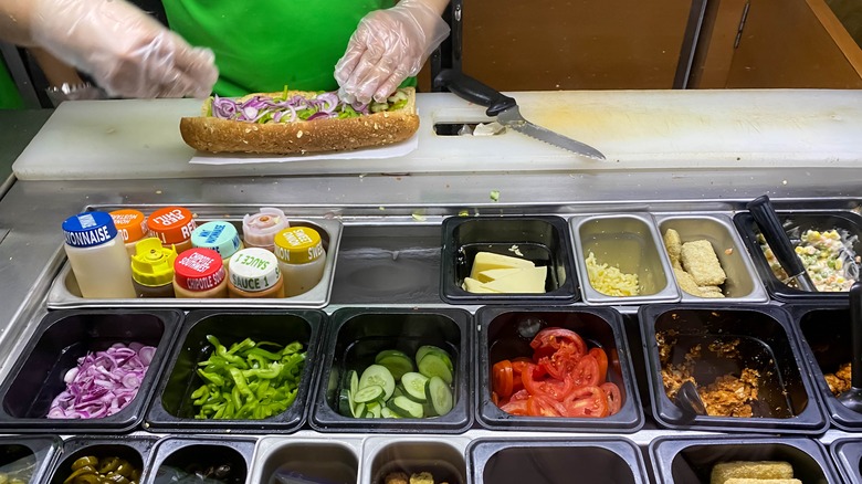 Subway Sandwich Artist putting veggies onto sandwich