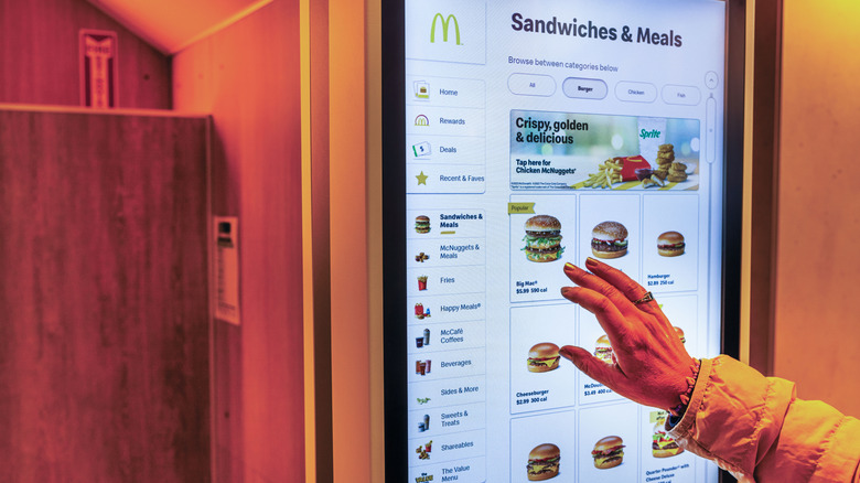 Person's hand touching kiosk screen at McDonald's