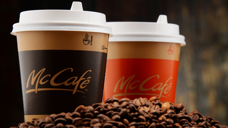 Two McCafe cups with lids among a pile of coffee beans