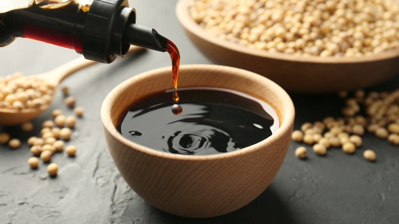 Bottle of soy sauce being poured into wooden bowl