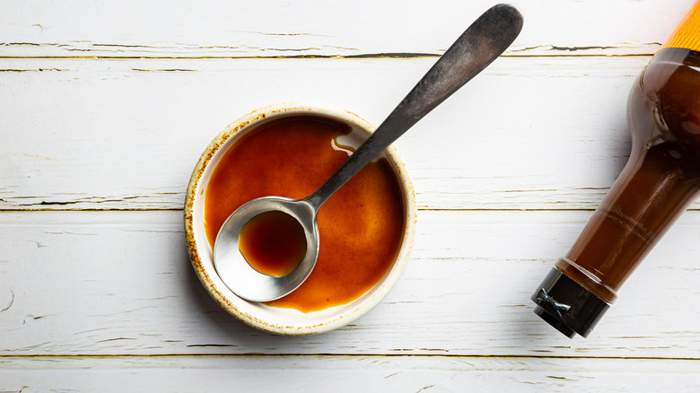 Bowl of Worcestershire sauce with a spoon and a bottle in the background