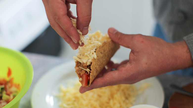 Person topping taco with shredded cheese