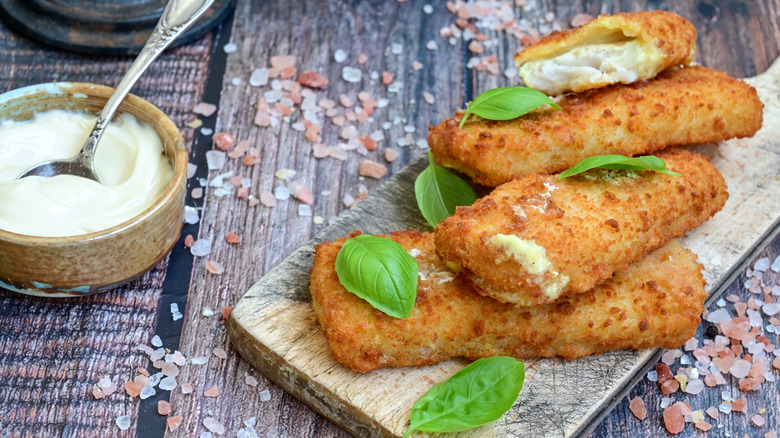 Crispy fried cod sticks on a wooden board with remoulade