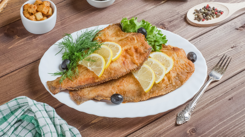 A plate of fried flounder topped with lemon slices