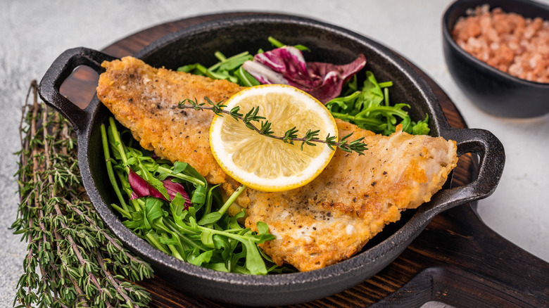 Fried haddock in a pan with salad and lemon