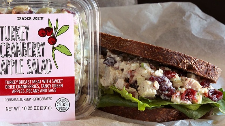Package of turkey cranberry apple salad next to sandwhich.