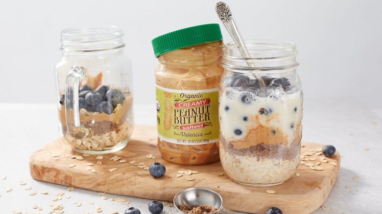 Trader Joe's peanut butter on cutting board with two mason jars of breakfast parfaits.