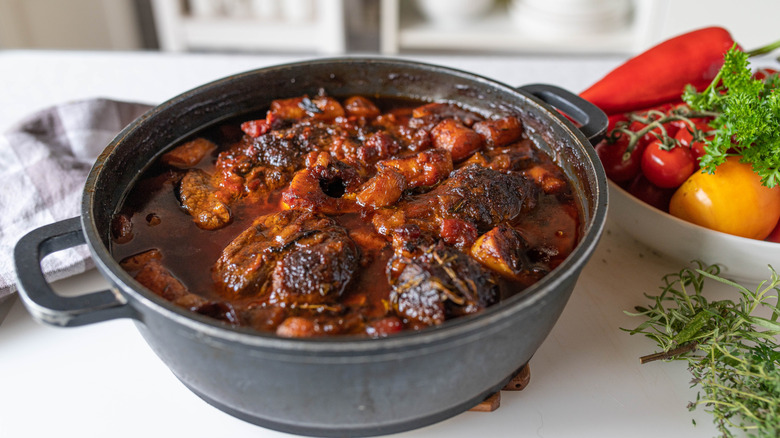 Braised meat in cast iron dish next to bowl of vegetables