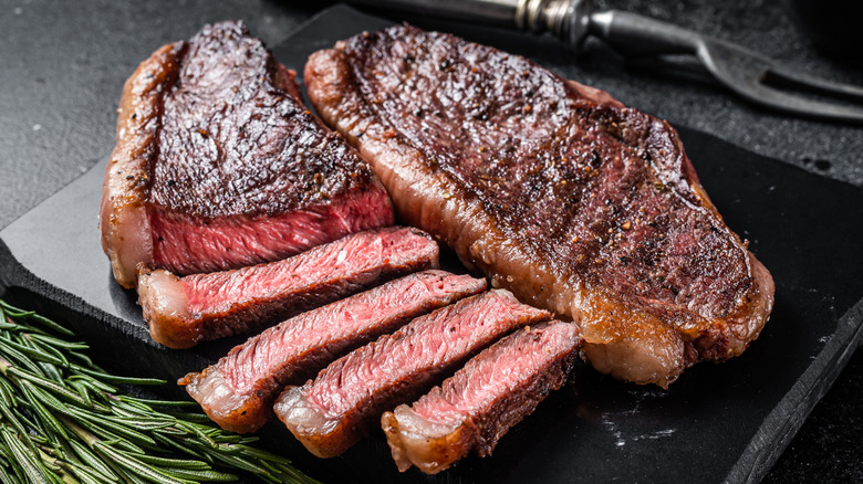 A medium rare strip steak sliced on a cutting board next to rosemary