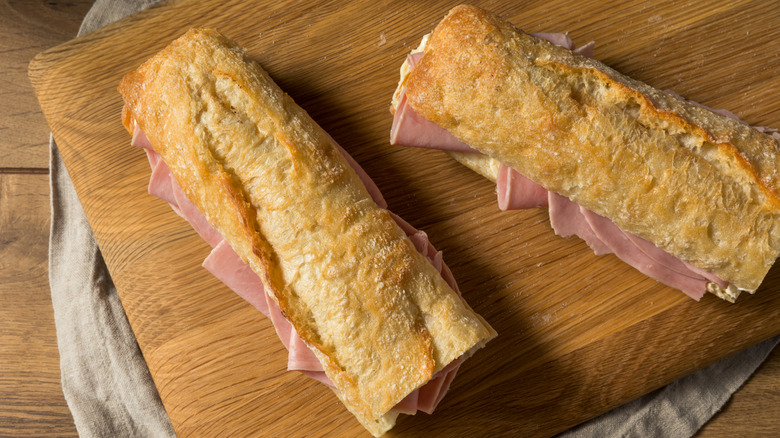 two jambon beurre sandwiches sit on a cutting board, made with crisp baguettes