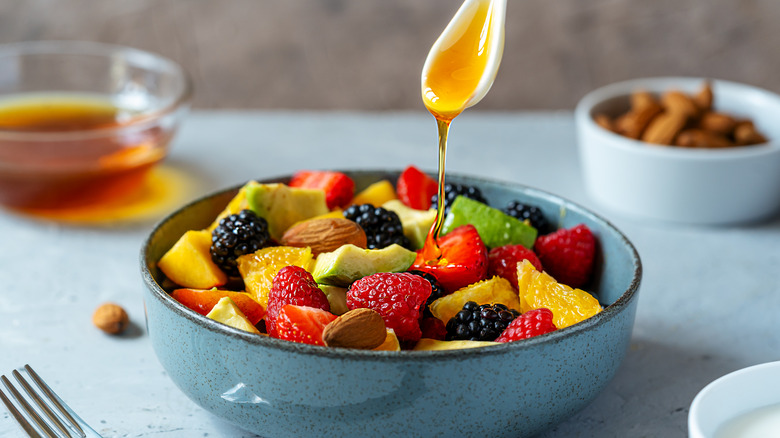 Spoon drizzling honey over a bowl of fruit salad