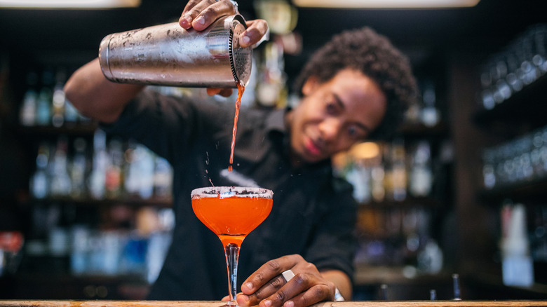 A bartender straining a chilled cocktail into a coupe glass
