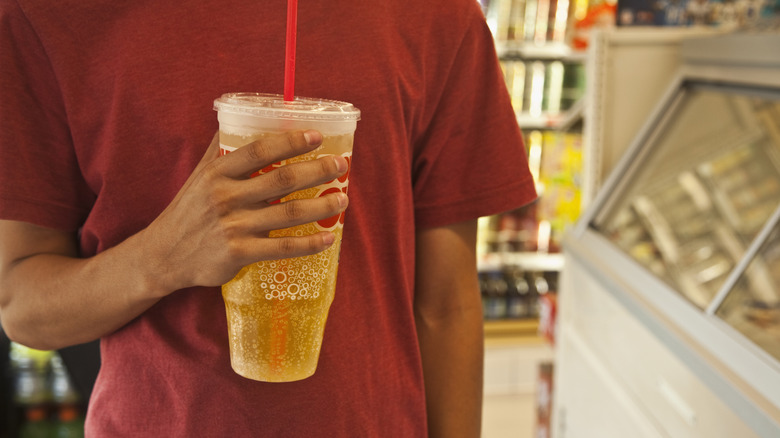 Man holding a very large plastic cup of soda in a convenience store
